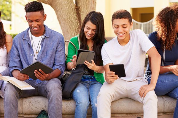 Young students checking their phones and other devices, something educators can incorporate into instructional design