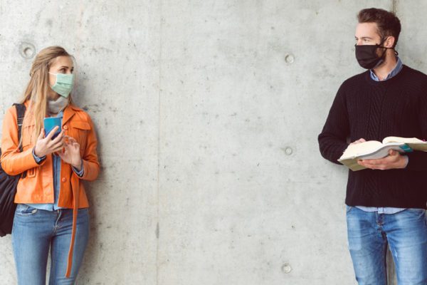 Two masked college students social distancing