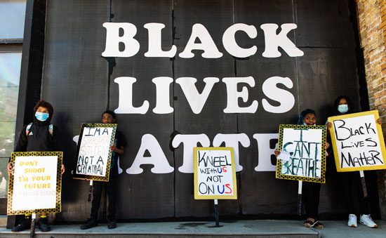 Protestors with signs in front of wall with "BLACK LIVES MATTER" on it