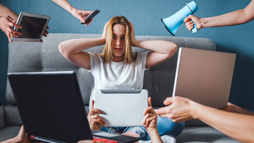 Woman overwhelmed by news all around her in the form of tablets, laptops, a phone, and a megaphone