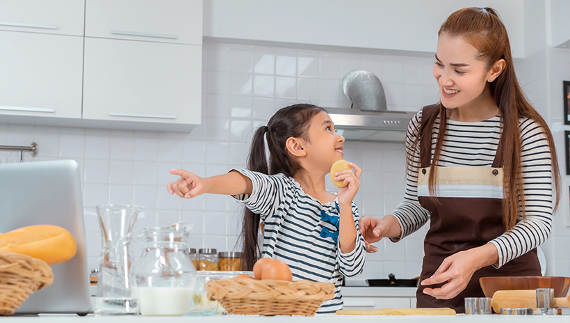 Mother and child baking bread together as part of a virtual event; child points to laptop