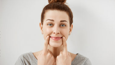 Teacher using her fingers to make her mouth smile, representative of maintaining a positive mindset