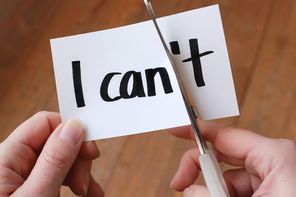 Scissors cutting slip of paper with "I can't" in such a way that it reads "I can," representing staying motivated