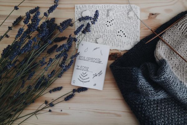 Zines on a wooden table, between flowers and a handbag